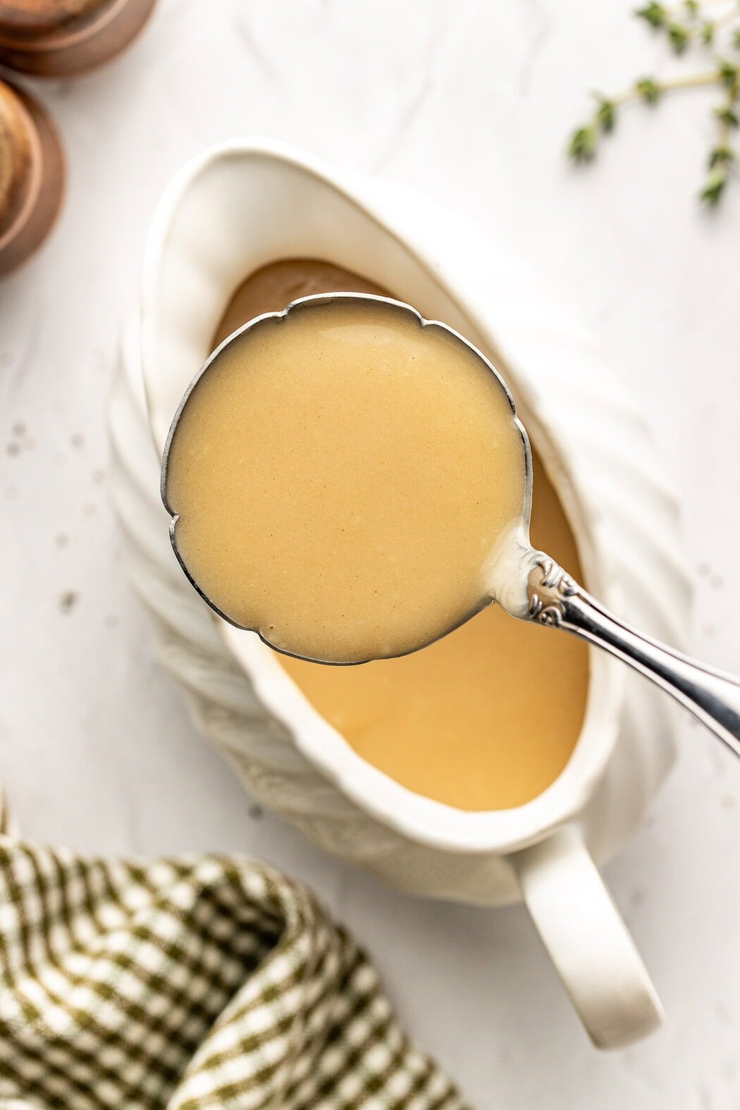 Overhead view of a ladle filled Turkey Gravy from a white gravy boat below. 