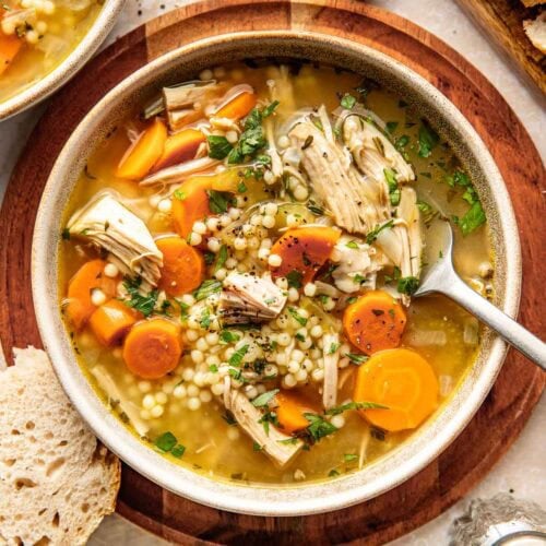 Overhead view of a bowl of turkey soup topped with fresh herbs and black pepper.
