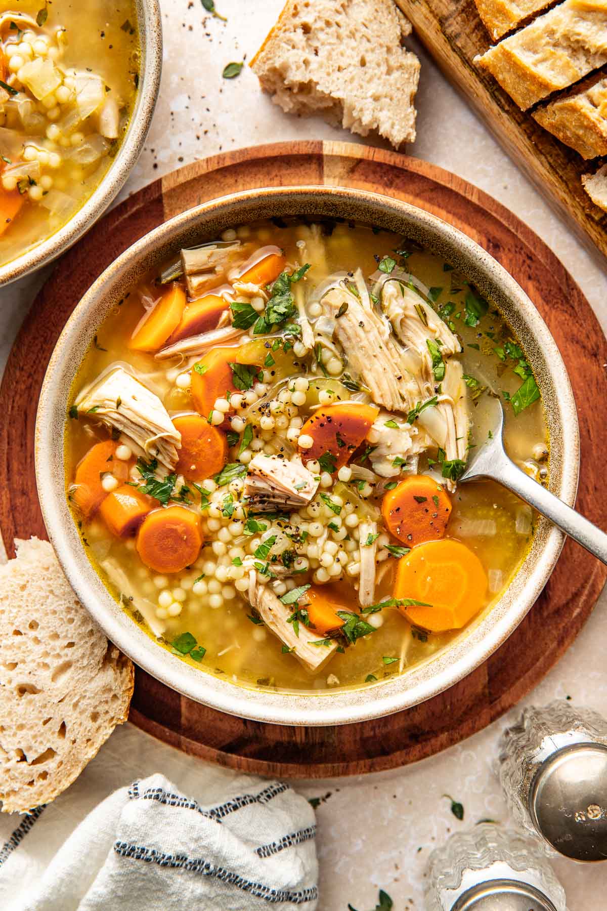 Overhead view of a bowl of Turkey Soup topped with fresh herbs and black pepper with bread pieces on the side.