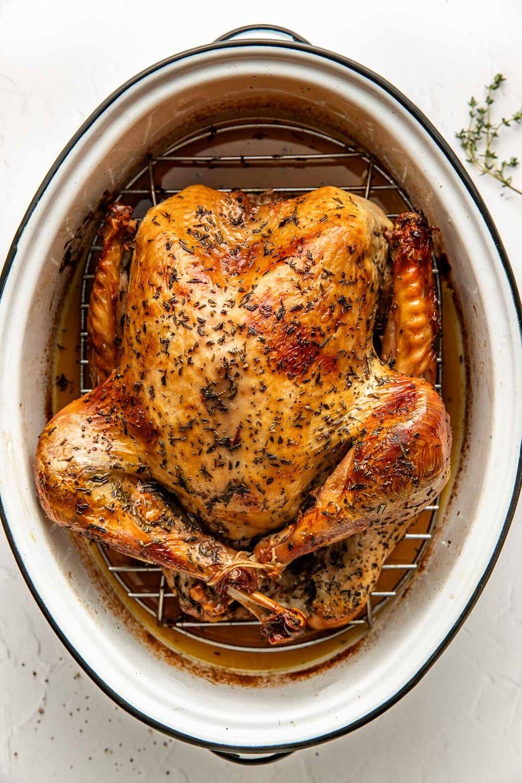 Overhead view of a freshly roasted turkey in a roasting pan on a rack surrounded by drippings. 