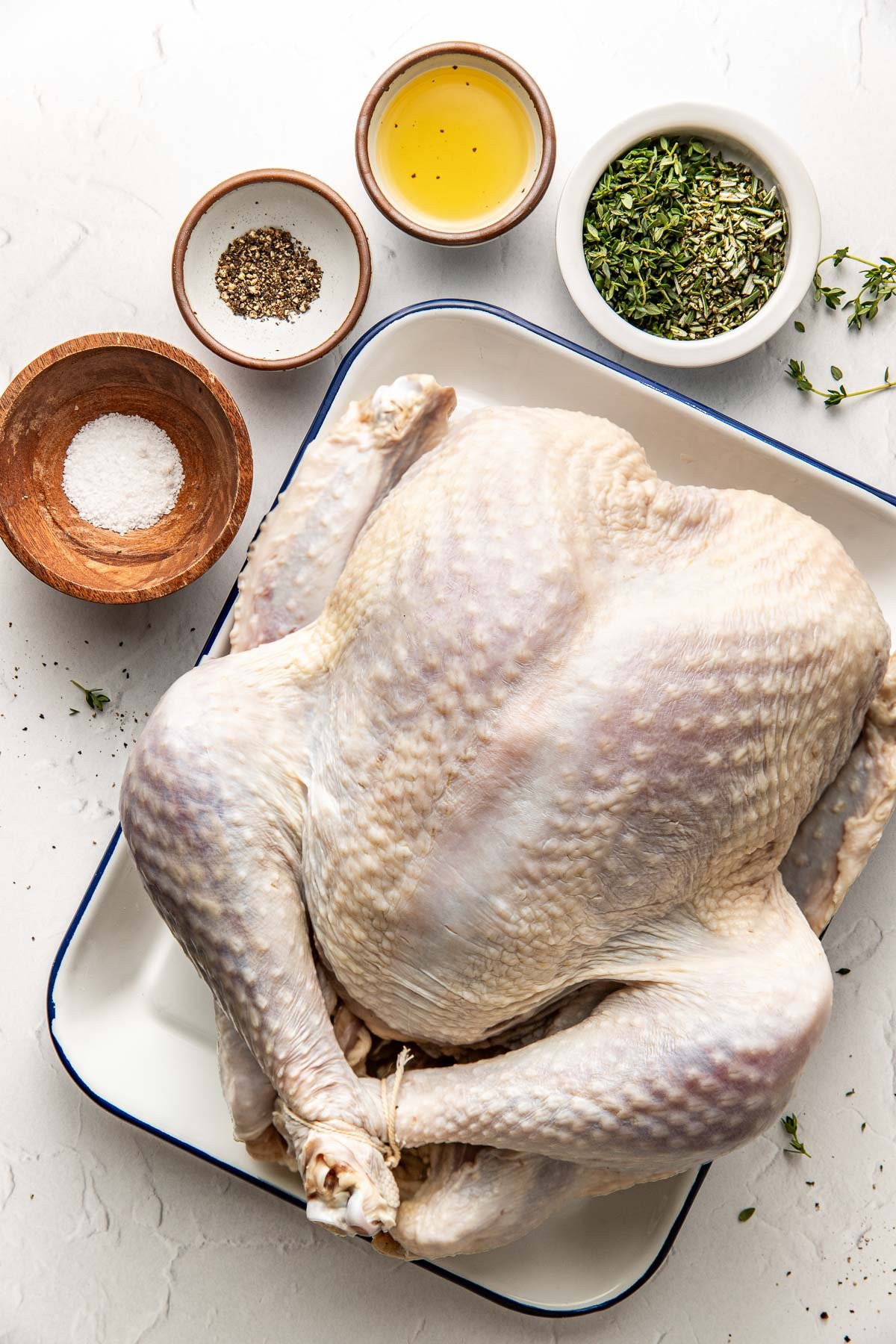 Overhead view of a raw turkey in a pan with fresh herbs and seasonings on the side. 