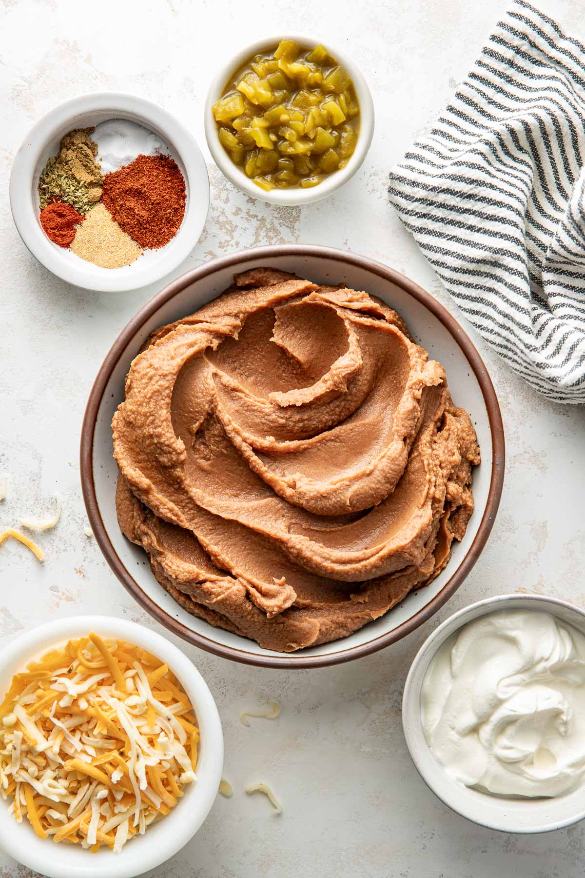 Overhead view of a variety of ingredients for Homemade Bean Dip in different sized bowls including refried beans.