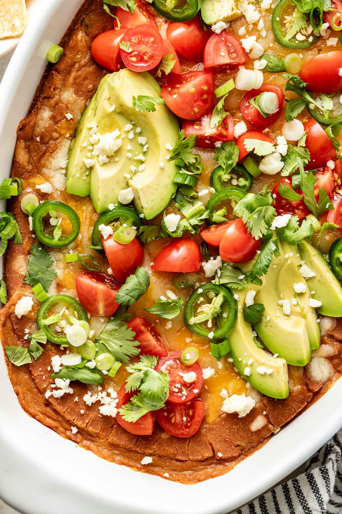 Close up view of the top of a freshly baked dish of Homemade Bean Dip topped with fresh cilantro, tomatoes, and sliced jalapeno.