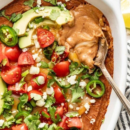 Overhead view of an oval baking dish filled with bean dip and topped with avocado, jalapeno, and diced tomatoes.