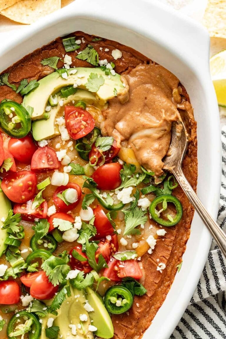 Overhead view of a baking dish filled with bean dip topped with avocado slices and diced tomatoes.