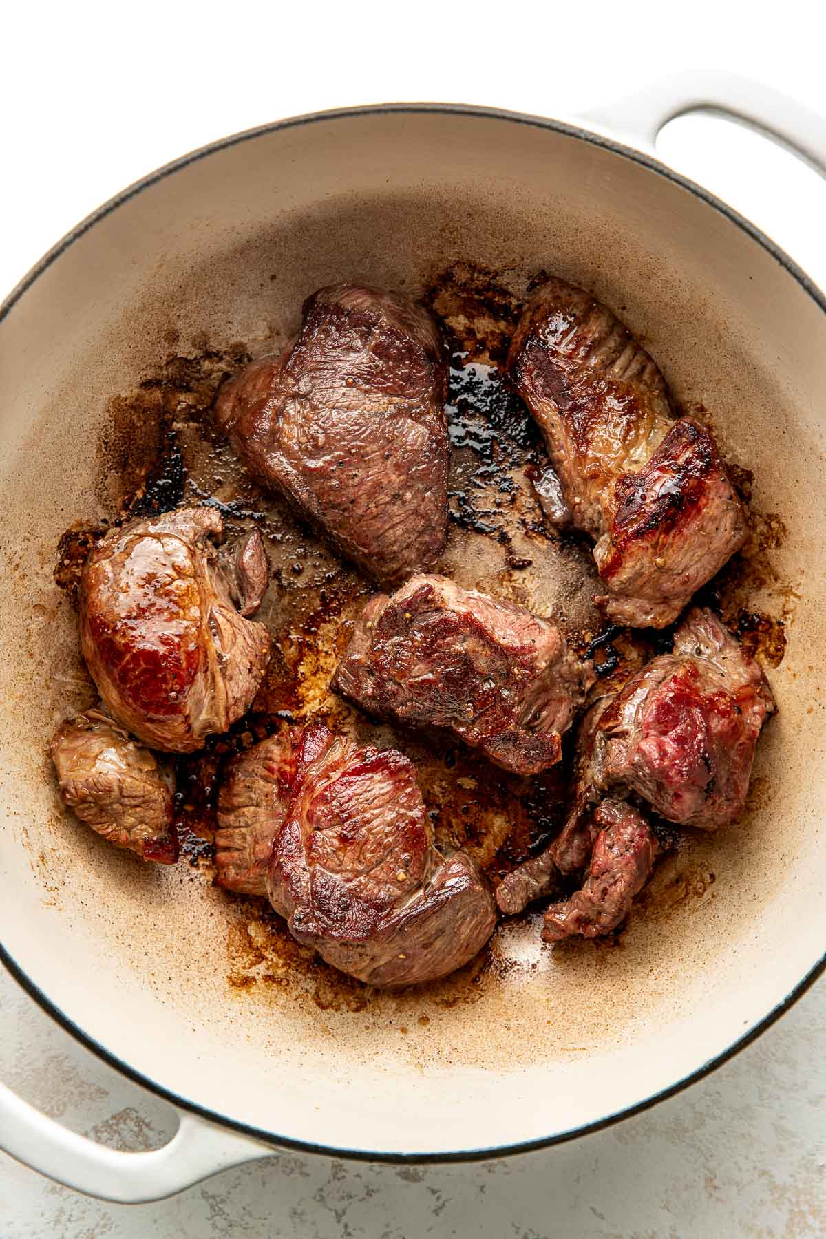 Overhead view of a white skillet filled with seared pieces of beef ready to be added to a braise pan for ragu.