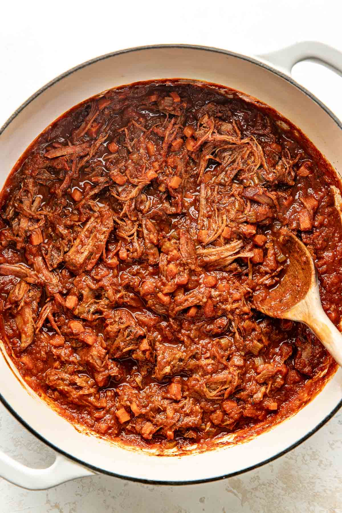 Overhead view of a white skillet filled with a beef ragu mixture ready for noodles to be added.