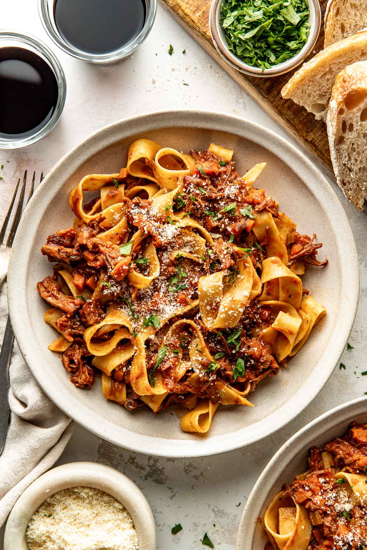Overhead view of a plate of Oven-Braised Beef Ragu topped with parmesan cheese and fresh herbs.