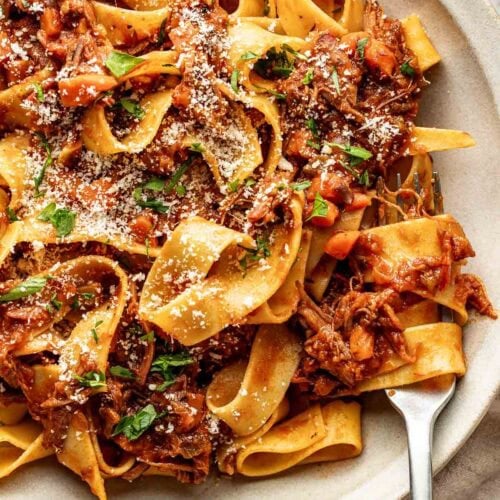 Close up view of a plate of Oven-Braised Beef Ragu topped with parmesan cheese and fresh herbs.