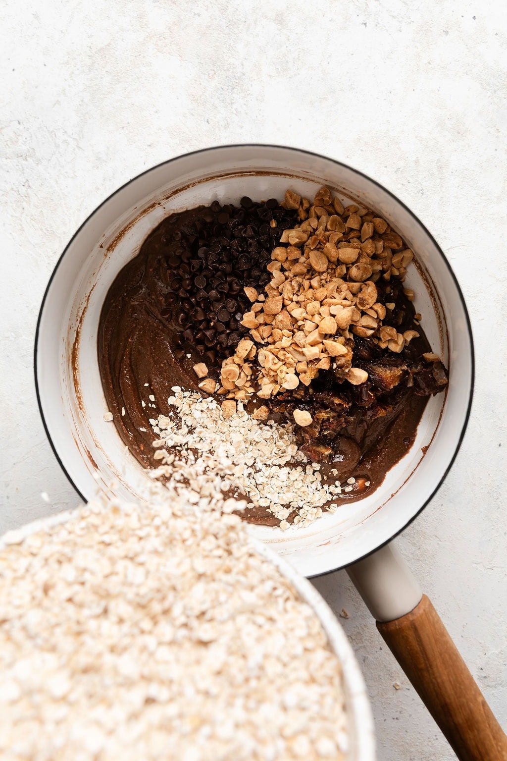 Overhead view of a pot with cookie ingredients and oats being poured into the mixture. 