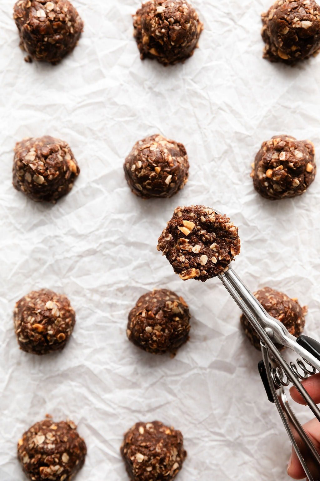 Overhead view of a cookie scoop putting no bake cookie dough on parchment paper. 