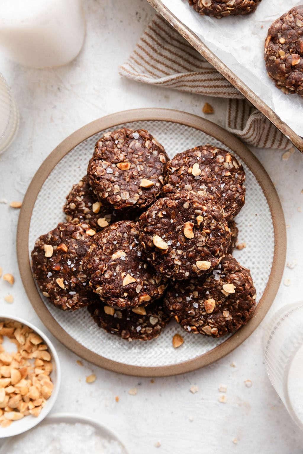 Overhead view of a plate of no bake cookies topped with flakey sea salt and chopped nuts. 