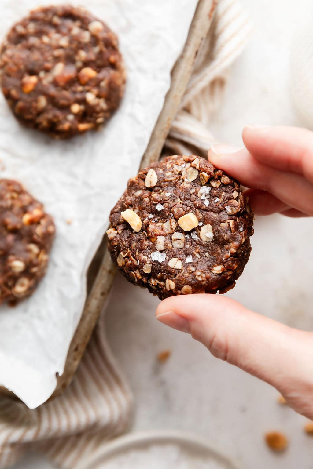 Overhead view of a hand holding a no bake cookie topped with flakey sea salt and chopped nuts. 