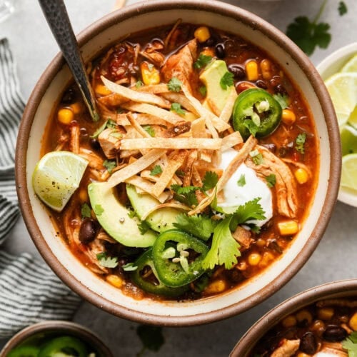 Overhead view of a bowl filled with Chicken Tortilla Soup topped with sliced jalapenos and garnished with limes.