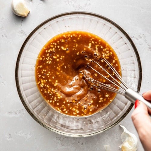 Overhead view of a glass bowl of stir fry sauce being mixed with a whisk.