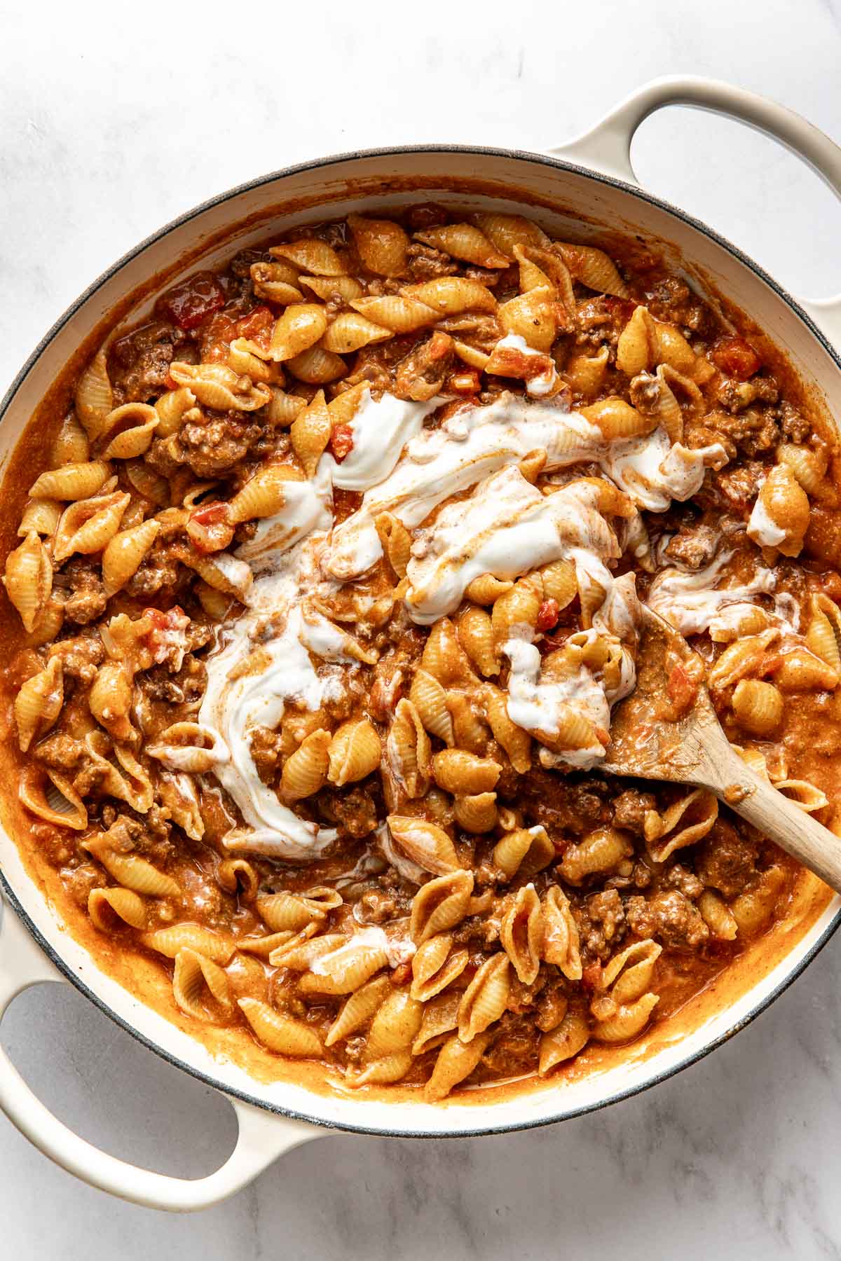 Overhead view of a white skillet filled with Taco Pasta being stirred with a wooden spoon.