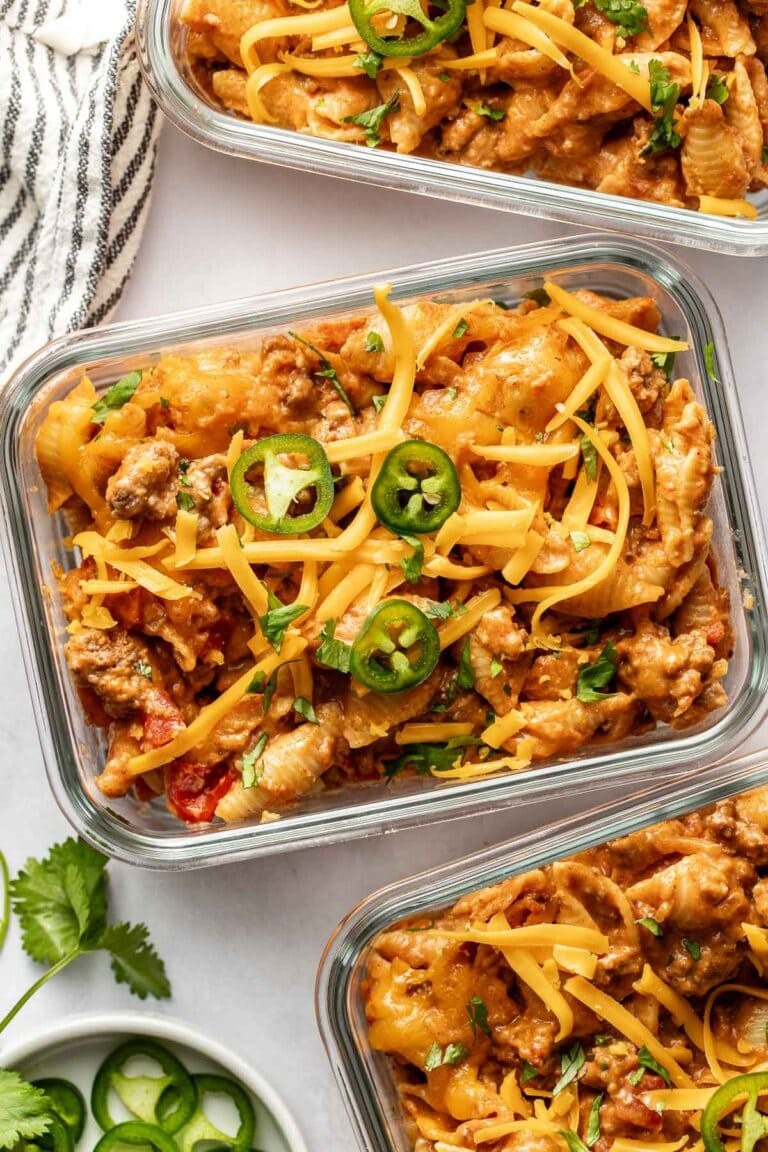 Overhead view of three glass meal prep containers filled with taco pasta topped with melted cheese and jalapeno slices.