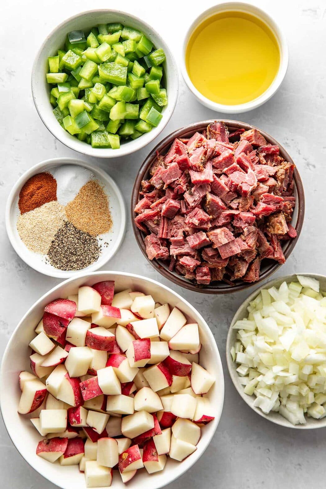 Overhead view of a variety of ingredients for Corned Beef Hash in different sized bowls.