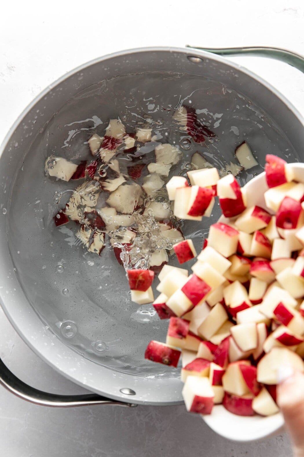 Overhead view of a pot of boiling water and diced potatoes being poured into the water.