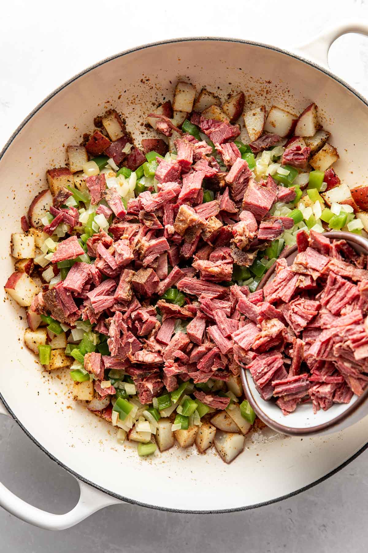 Overhead view of a skillet filled with Corned Beef Hash ingredients ready for stirring.