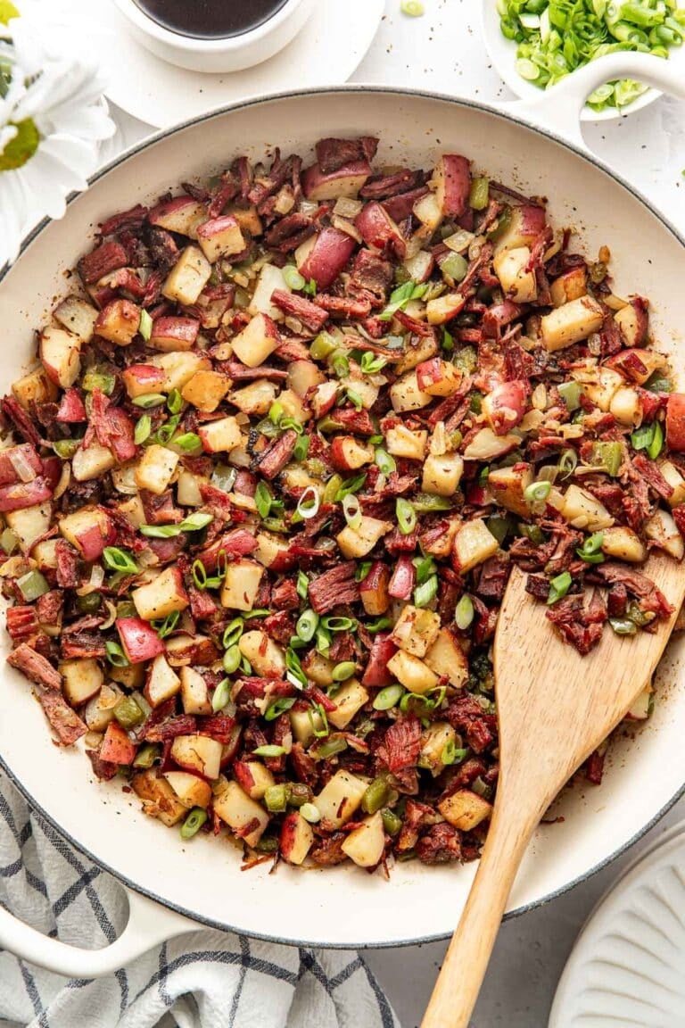 Overhead view of a white skillet filled with corned beef hash sprinkled with green onions.