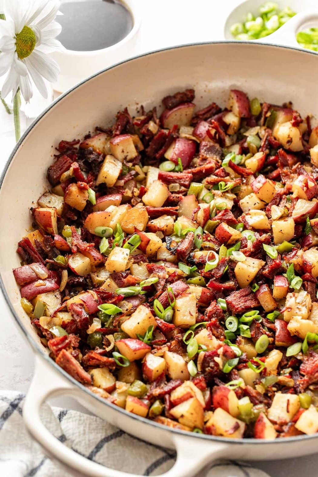 Close up view of a white skillet filled with Corned Beef Hash sprinkled with green onions.