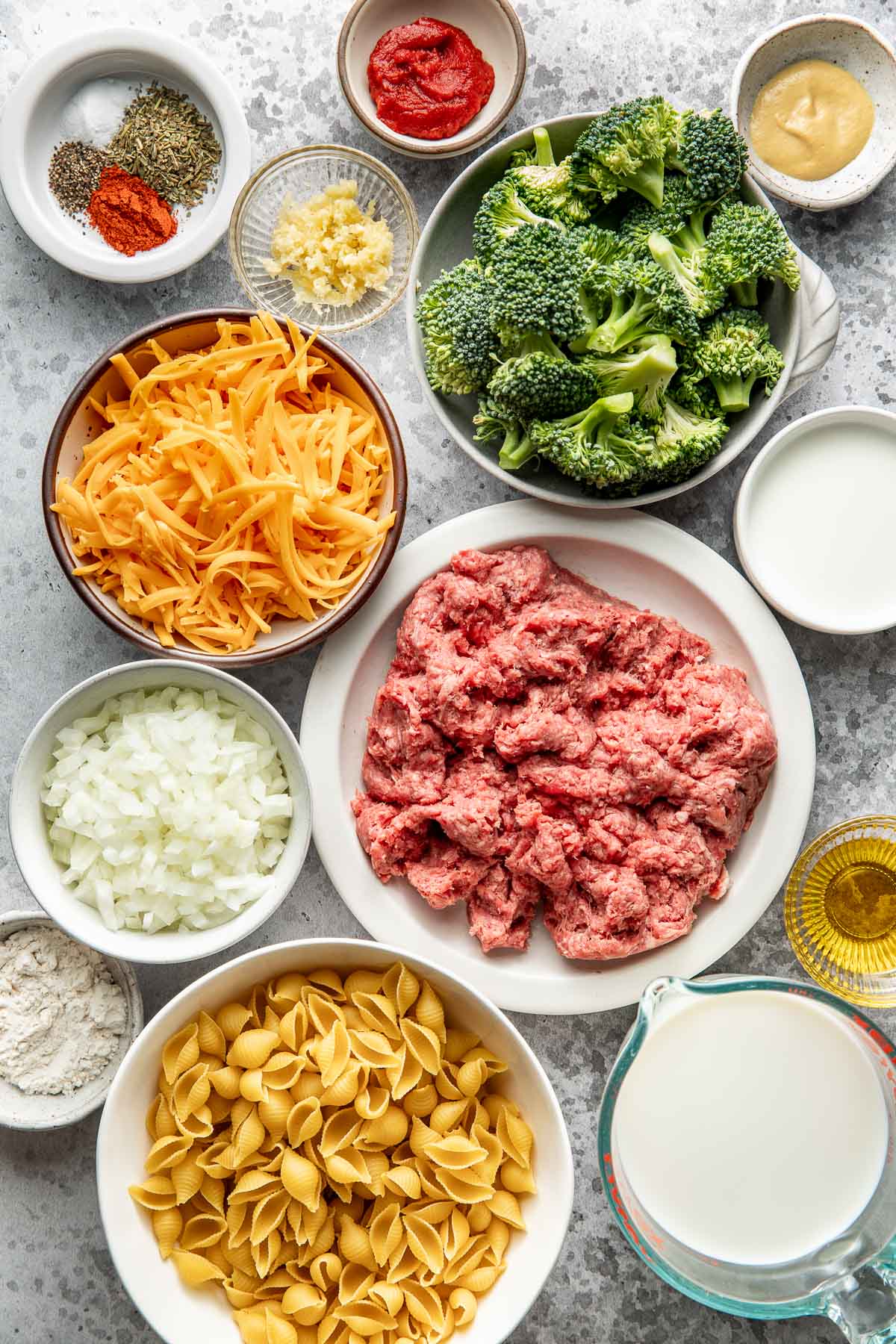 Overhead view of a variety of ingredients for Homemade Hamburger Helper in different sized bowls on a marble countertop.