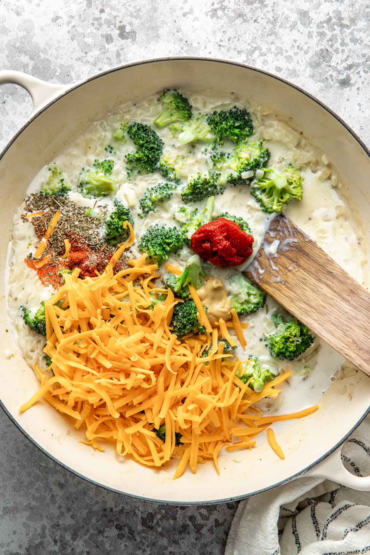 Overhead view of a skillet filled with broccoli, tomato paste, shredded cheese and spices.