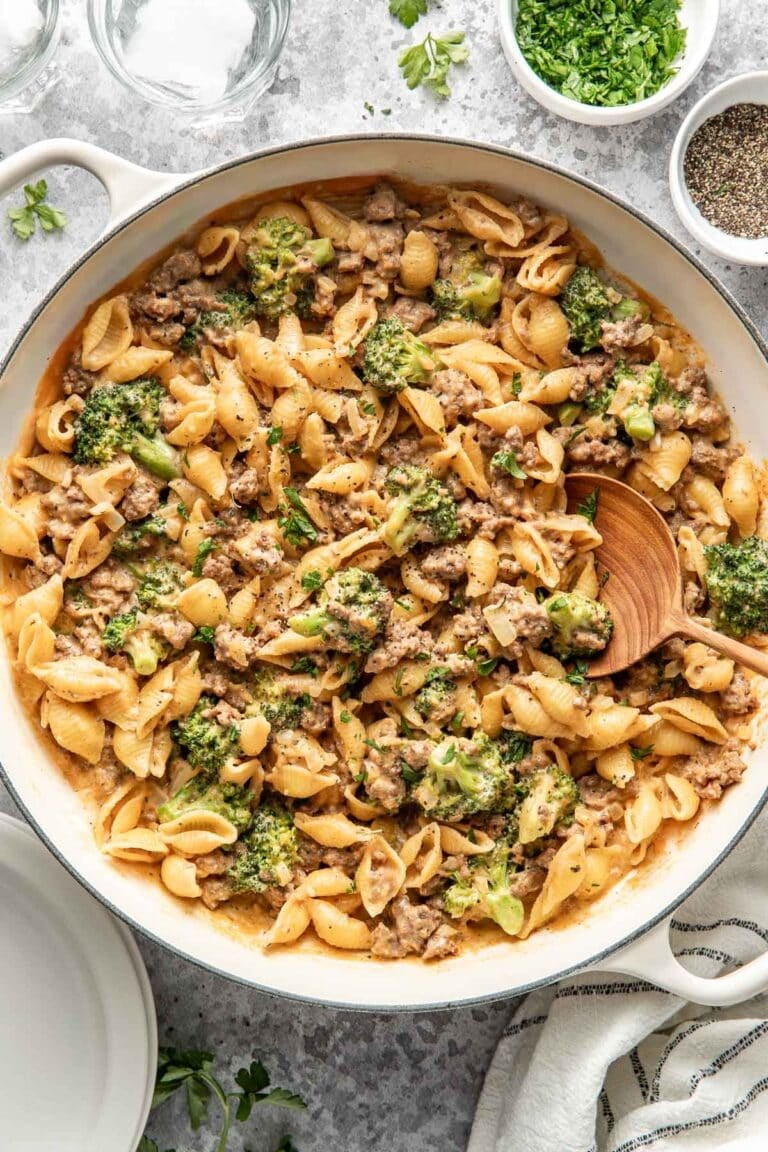 Overhead view of a white skillet filled with creamy homemade hamburger helper topped with black pepper and fresh herbs in a creamy cheese sauce.