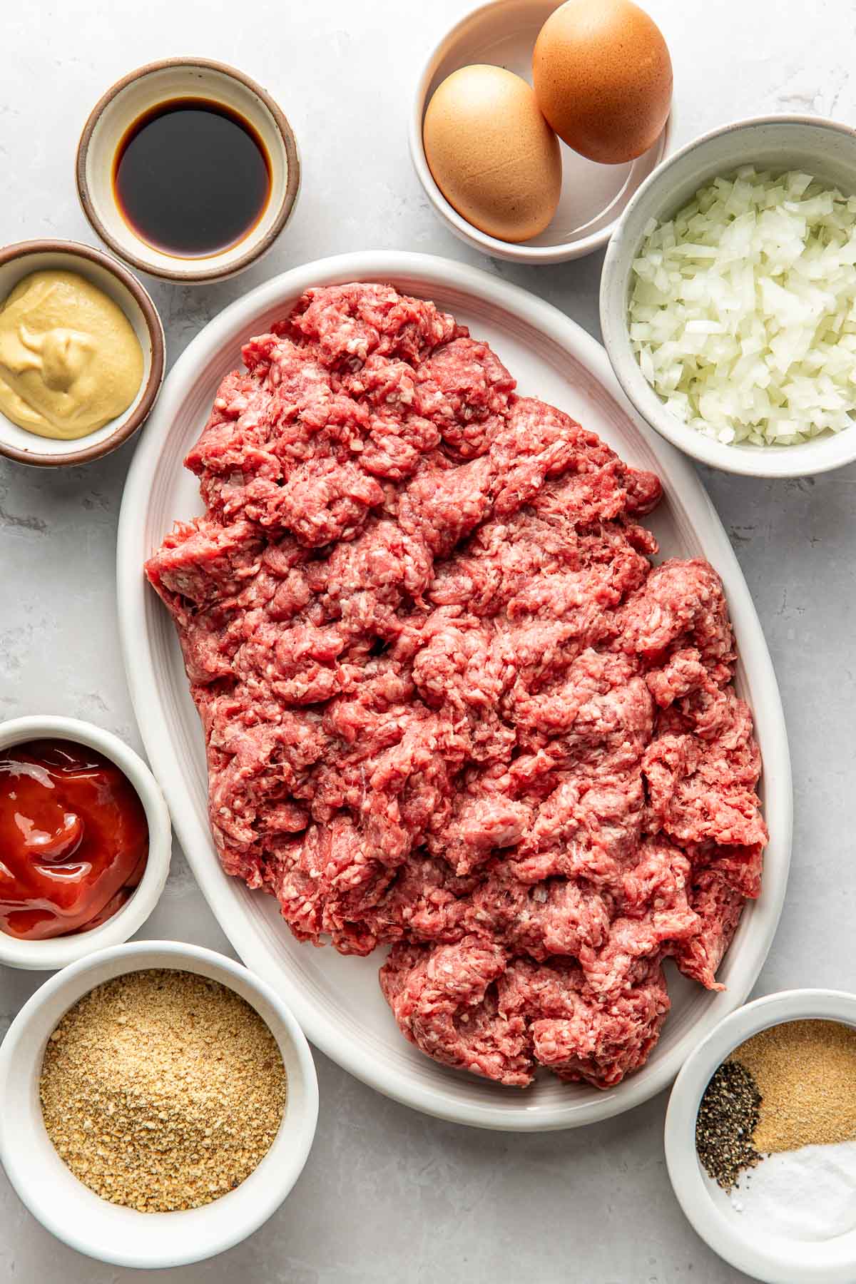 Overhead view of a variety of ingredients for Classic Meatloaf in different sized bowls.
