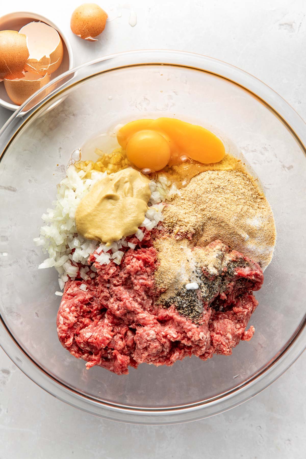 Overhead view of a glass mixing bowl filled with ingredients for meat loaf ready for mixing.