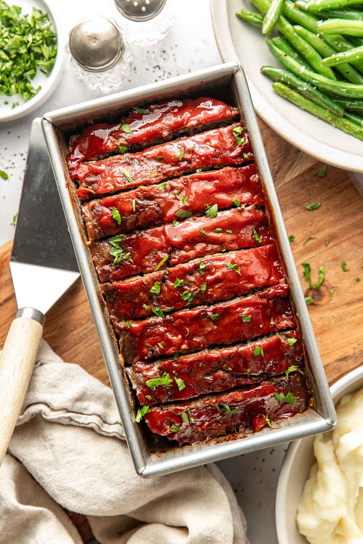 Overhead view of a loaf pan filled with freshly baked meat loaf topped with a tomato topping and sliced for serving.