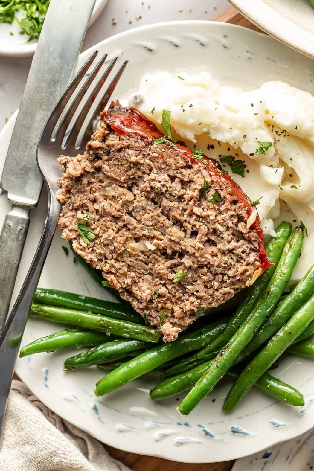 Close up view of a plate of mashed potatoes, Sautéed Green Beans, and a piece of meatloaf. 