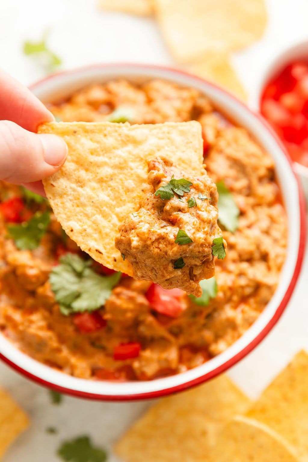 Close up view of a hand holding a tortilla chip dipped with Rotel Dip sprinkled with fresh cilantro.