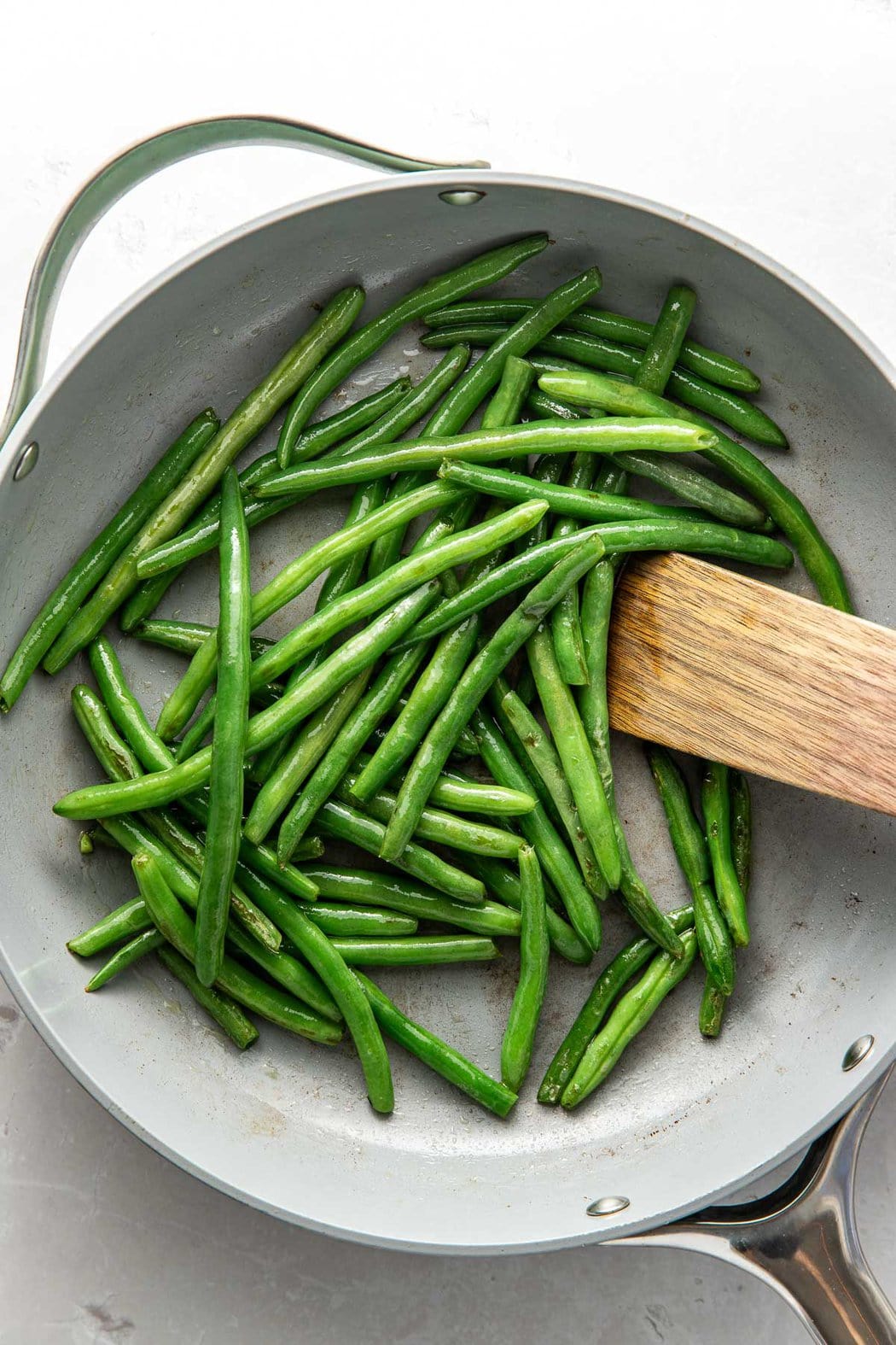 Overhead view of a pan filled with Sautéed Green Beans being stirred with a wooden spoon.