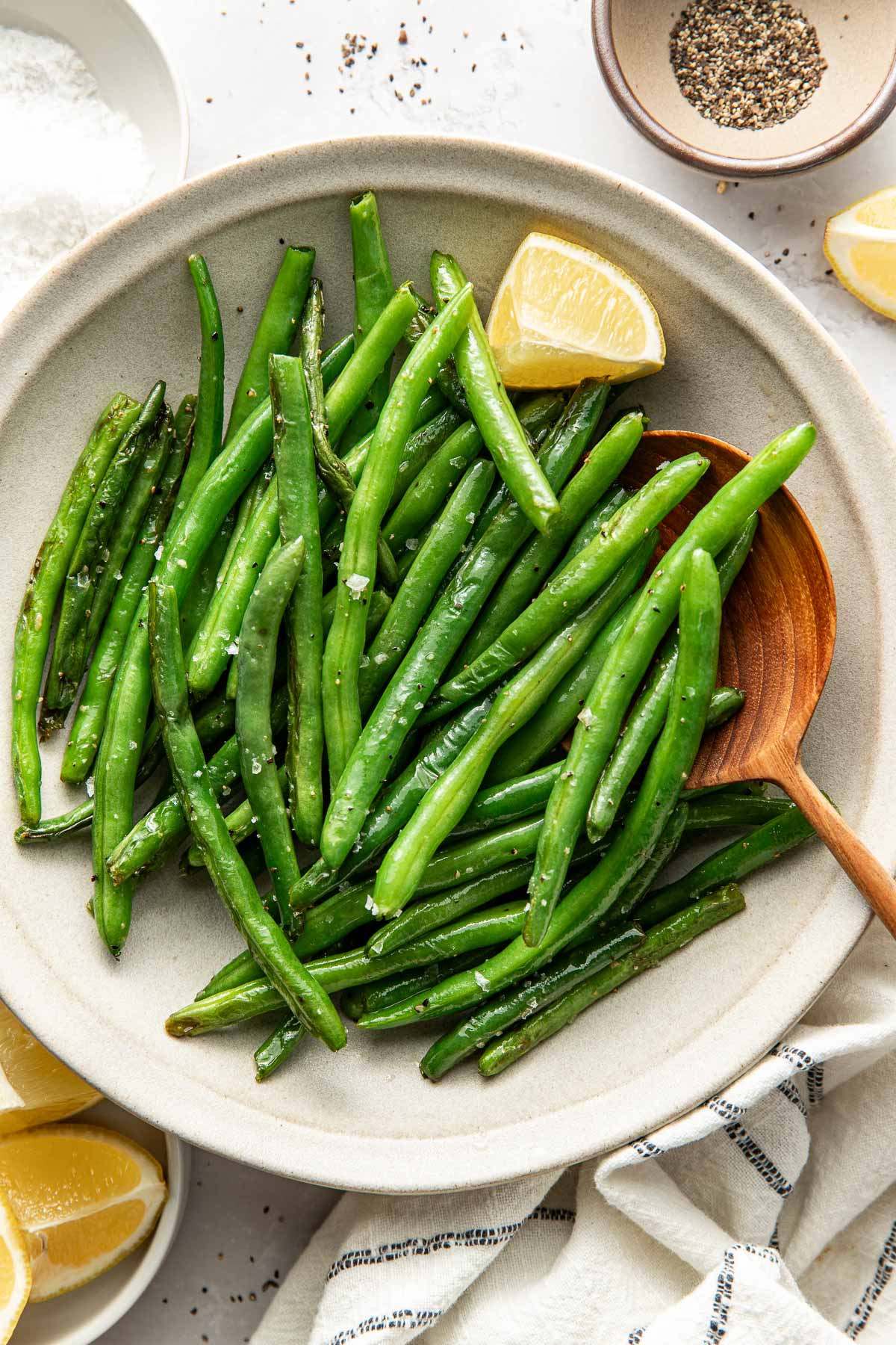 Overhead view of a bowl of Sautéed Green Beans topped with salt and pepper and garnished with a lemon wedge.