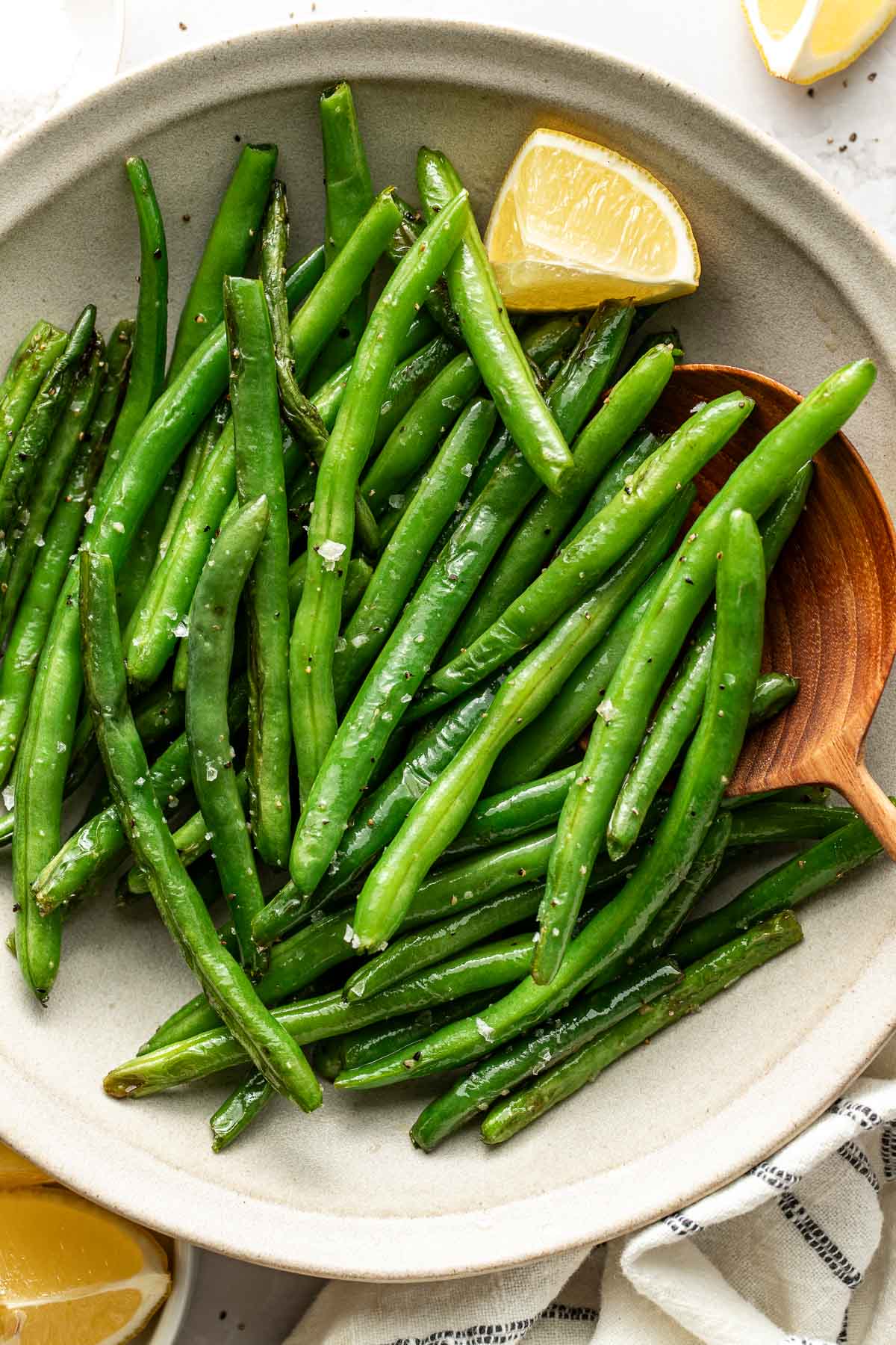 Close up view of a dish of Sautéed Green Beans sprinkled with flakey sea salt. 