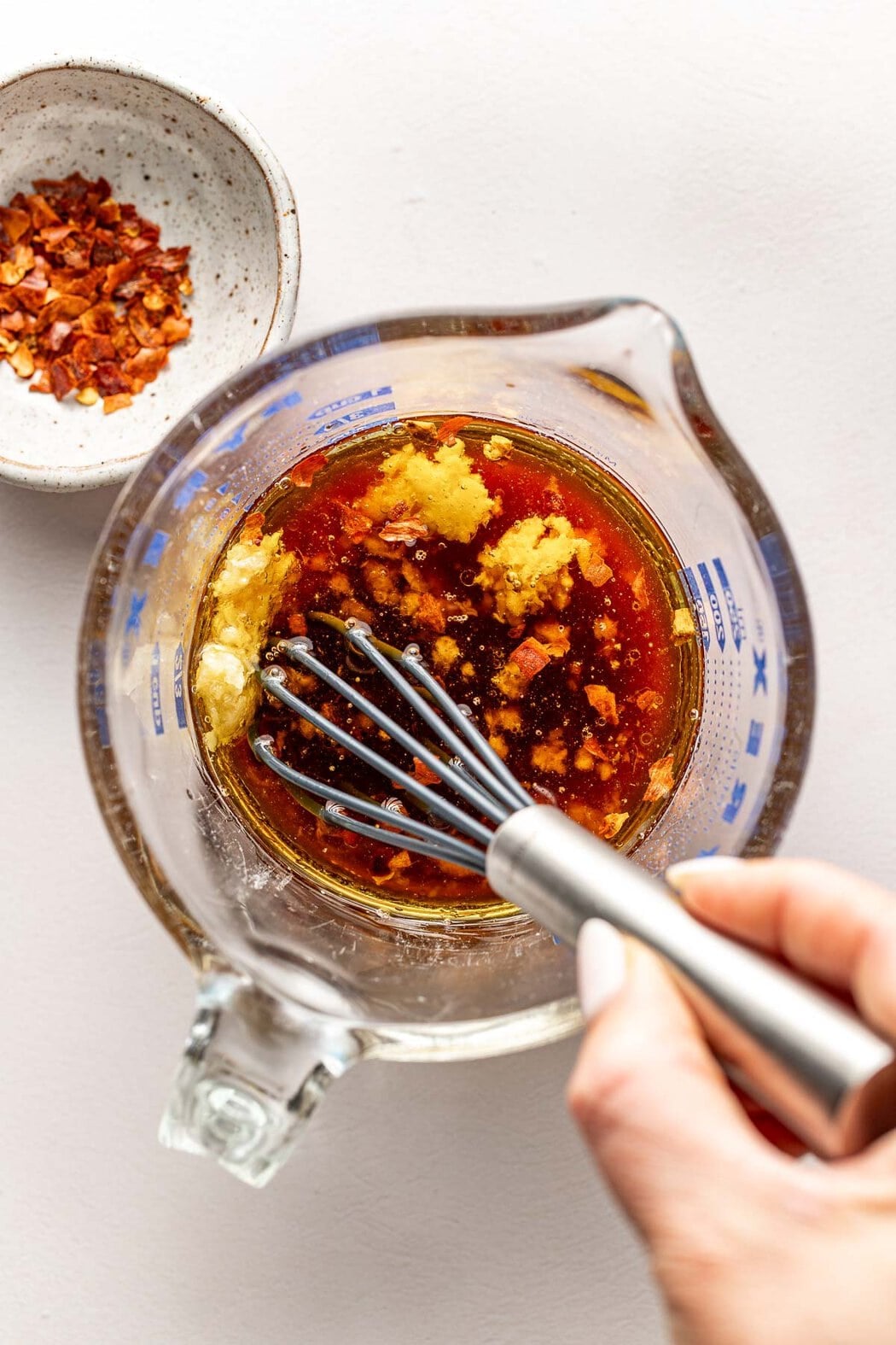 Overhead view of a glass measuring cup with a whisk stirring an Asian salad dressing.
