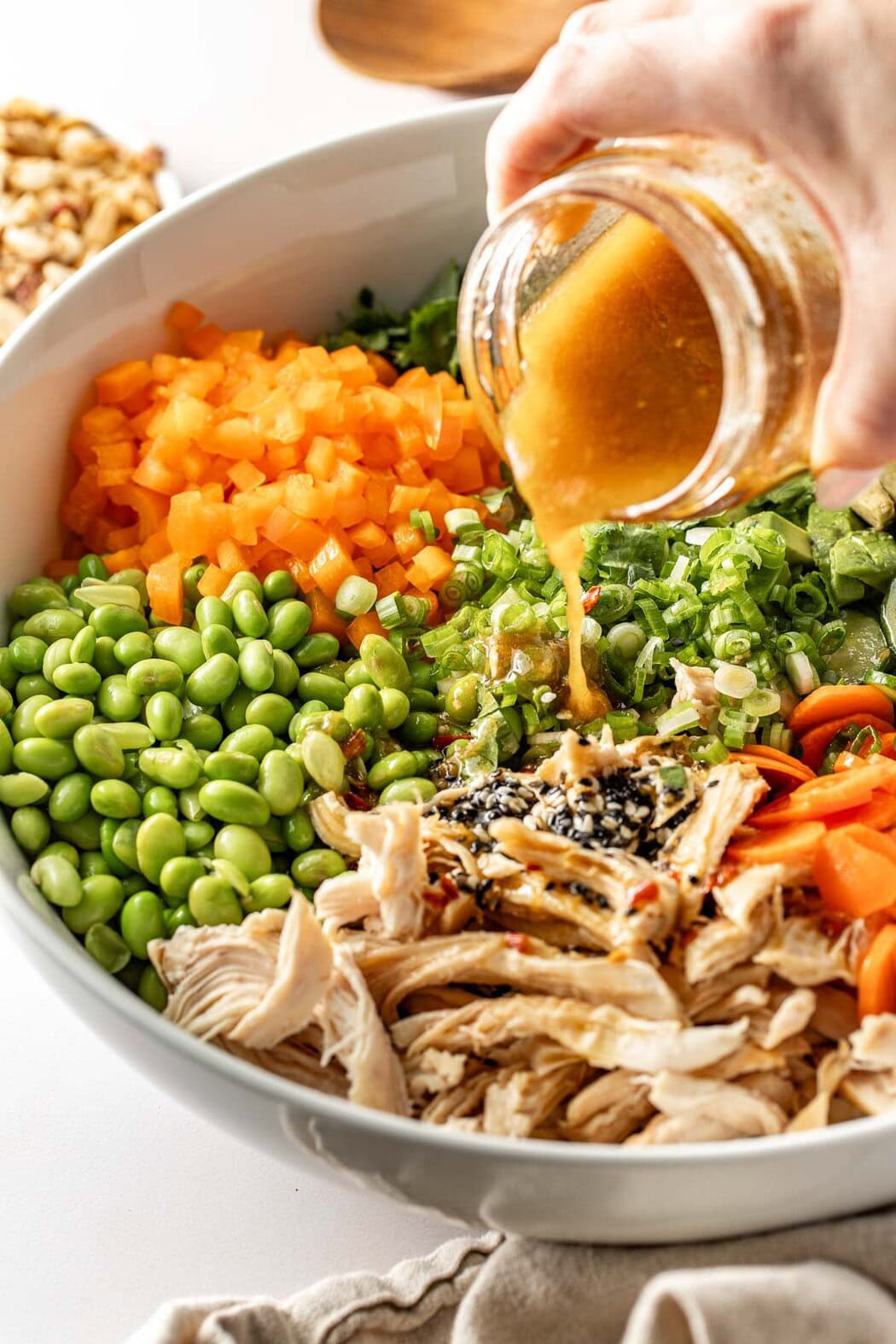 Close up view of a Thai Chicken Salad with a hand pouring an Asian dressing over the top.