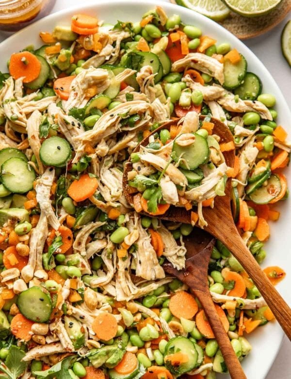 Overhead view of thai chicken salad in a white serving dish with wooden serving spoons