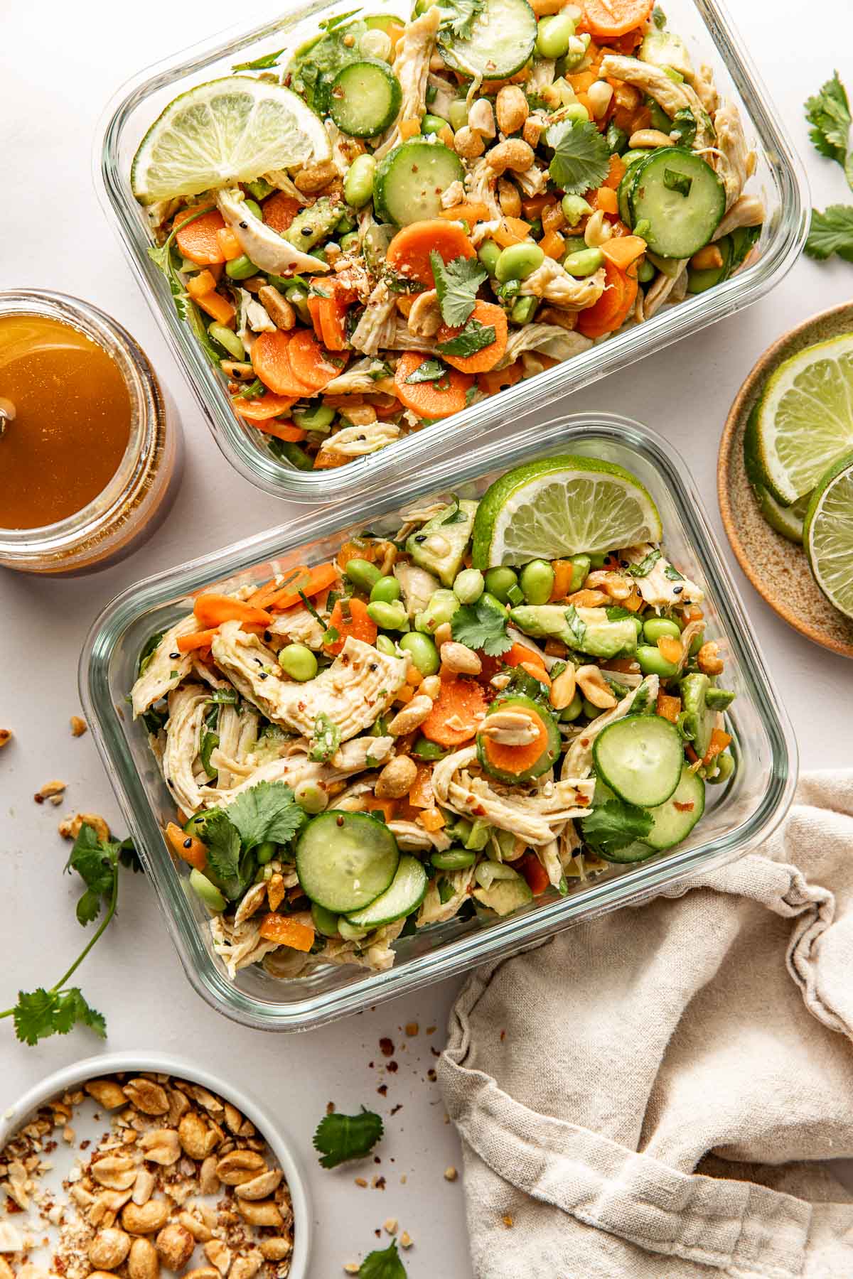 Overhead view of two glass meal prep containers filled with Thai Chicken Salad with Edamame and garnished with limes.
