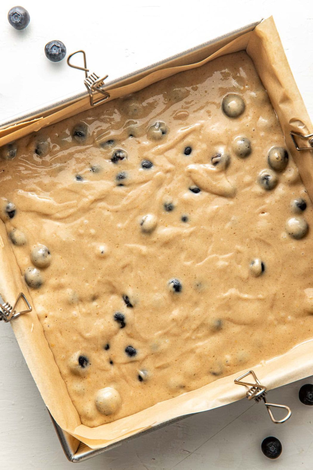 Overhead view of a 9x9 pan lined with parchment paper and filled with Blueberry Coffee Cake batter. 