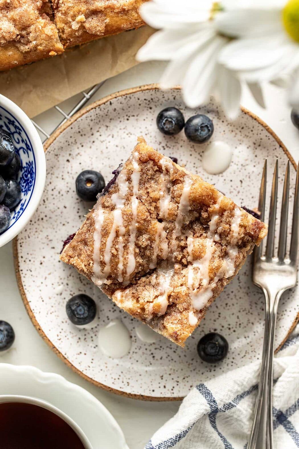 Overhead view of a plate with a square of Blueberry Coffee Cake on it, drizzled with an icing. 