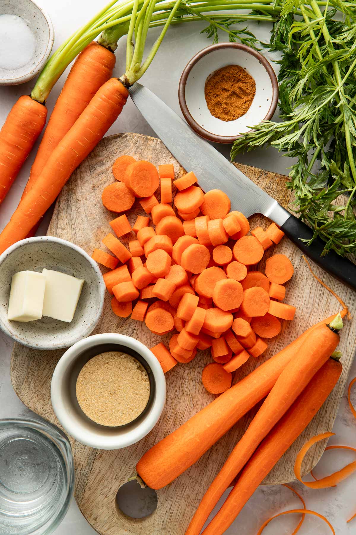 Overhead view of a wood cutting board surrounded by carrots and sliced carrots.