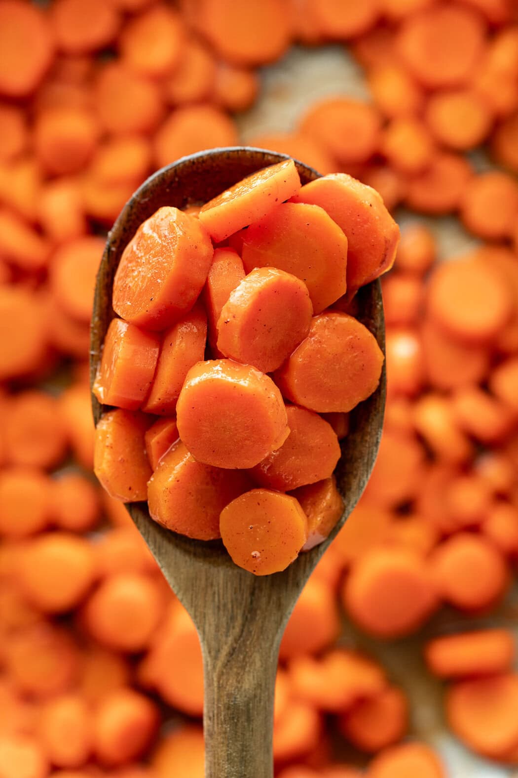 Close up view of a wooden spoon filled with sliced cooked carrots.