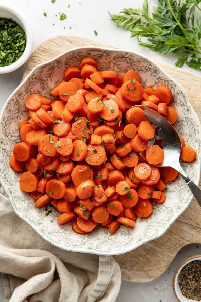 Overhead view of a bowl of candied carrots topped with fresh herbs and black pepper.