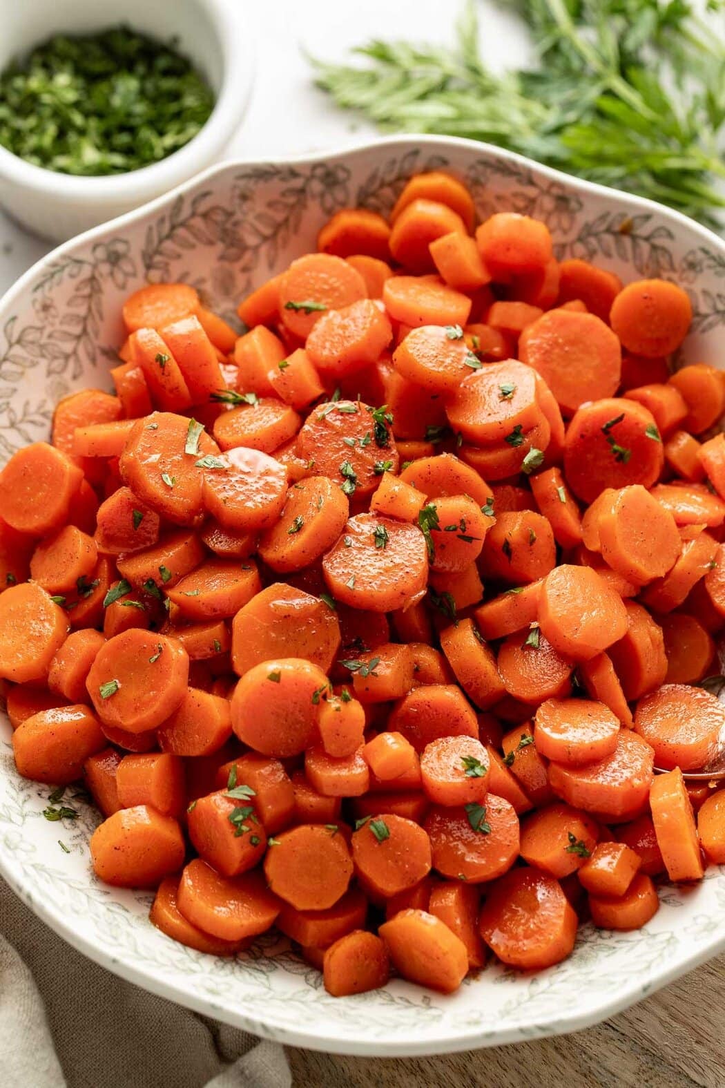 Close up view of a bowl filled with freshly cooked carrots topped with melted butter and fresh herbs.