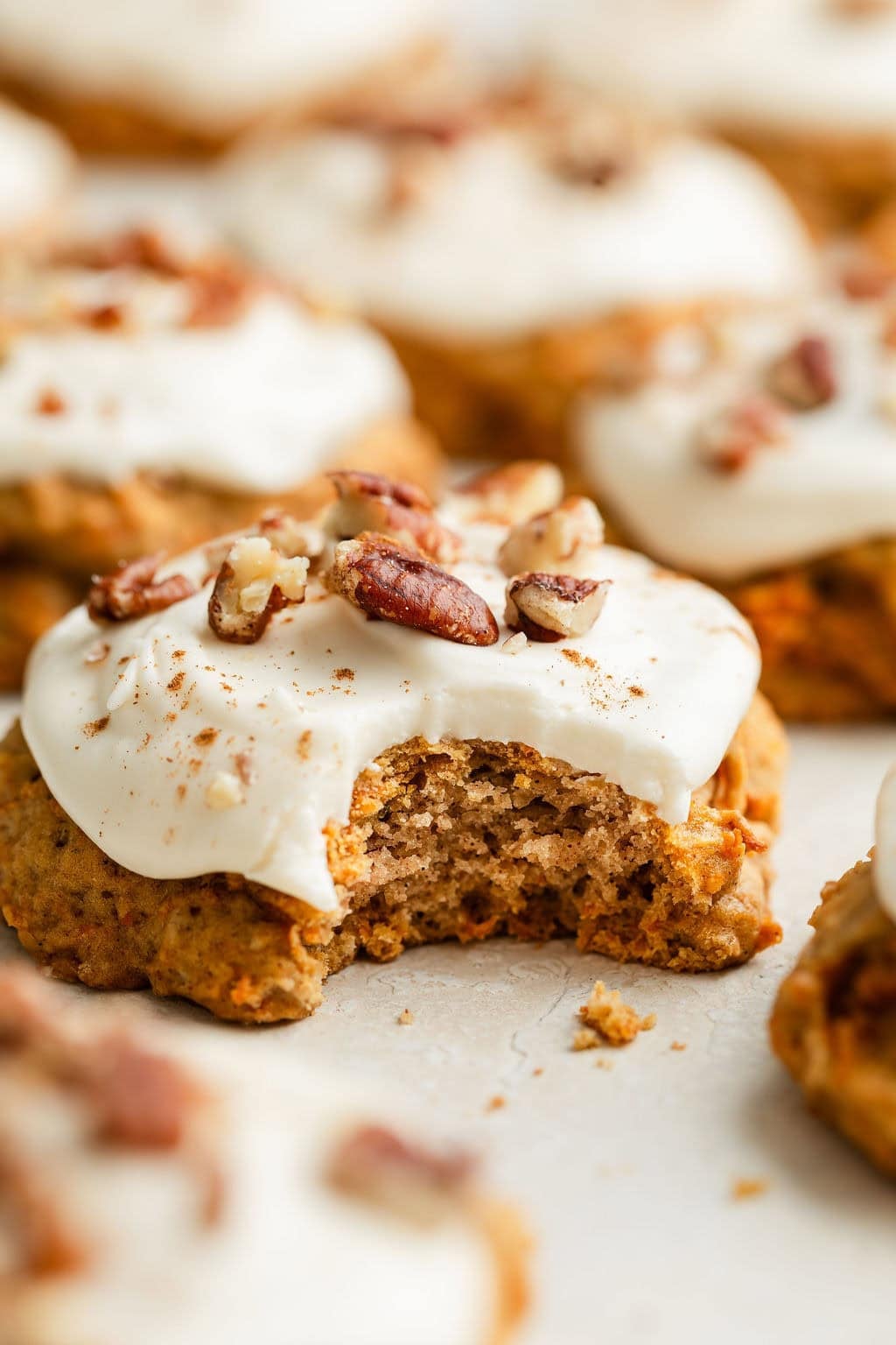 Close up view of a Carrot Cake Cookie topped with cream cheese frosting and sprinkled with pecan pieces and cinnamon. 