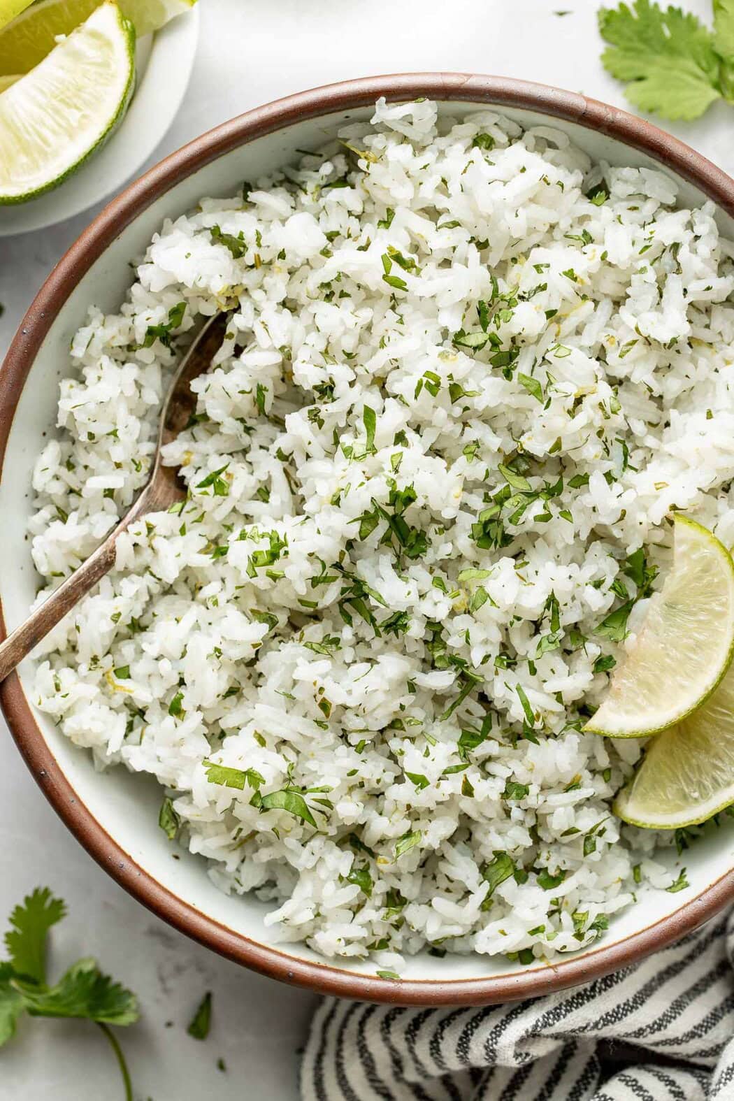 Close up view of a bowl of Cilantro Lime Rice topped with fresh cilantro and garnished with limes.