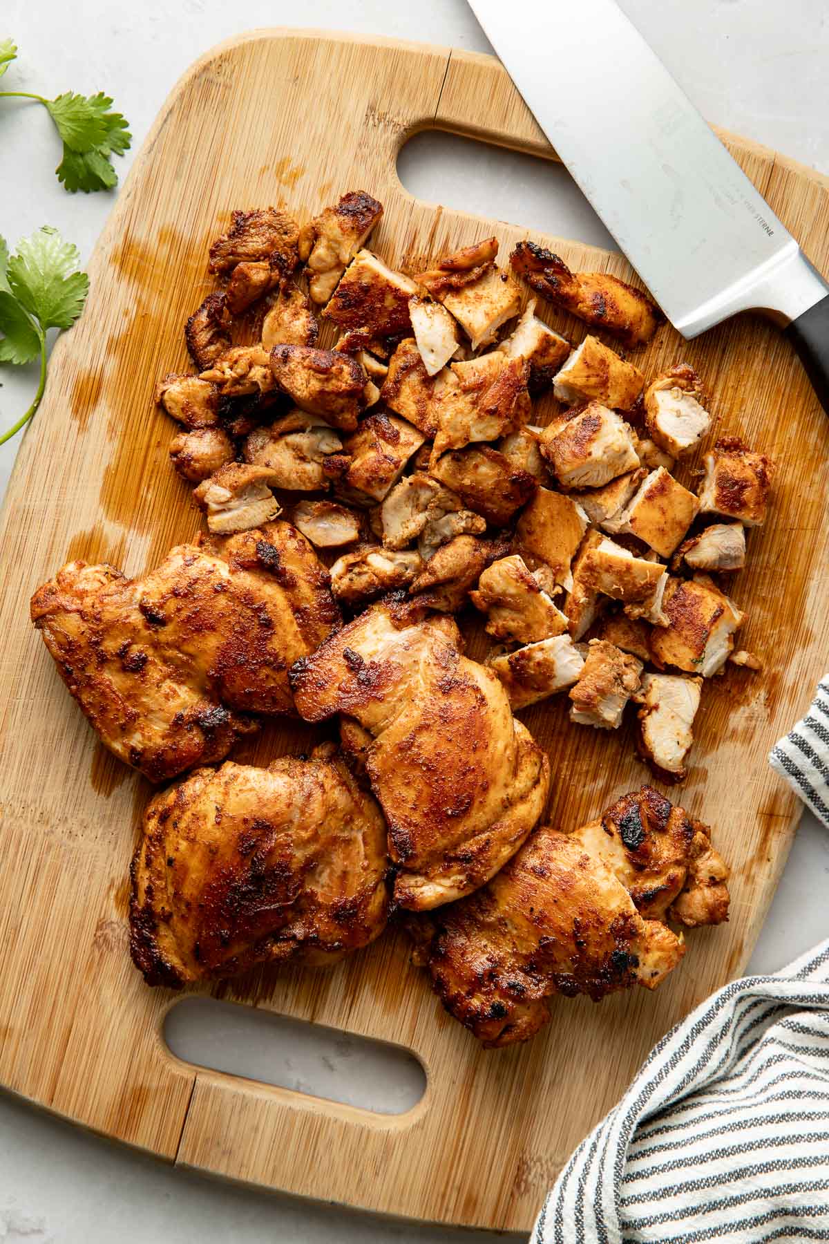 Overhead view of a wooden cutting board filled with cooked chicken thighs and some of the meat diced.